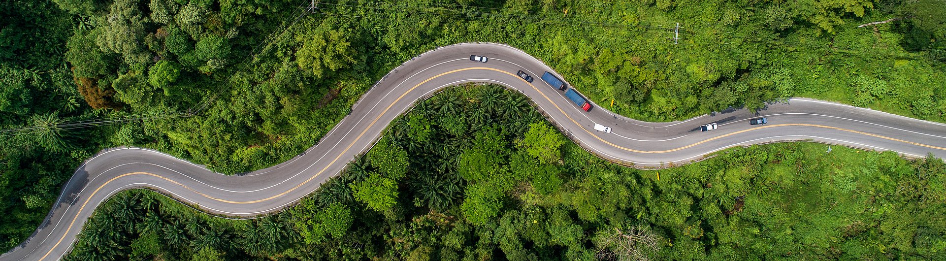 aerial view road curving through greenery up to mountain with cars
